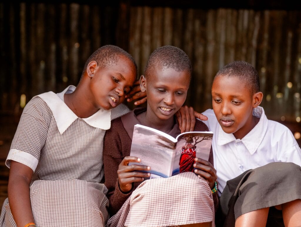 Three Brave Girls who found their refuge in Naning'oi Girls Primary School from FGM and Child Marriages read Brave, the power of choice, a book by Sarah Davies that is inspired by their stories. © Billy Miaron